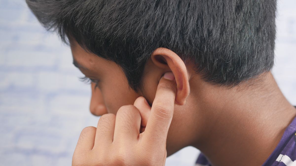 Profil d'un adolescent, la main posée sur l'oreille, à l'endroit de l'implant cochléaire